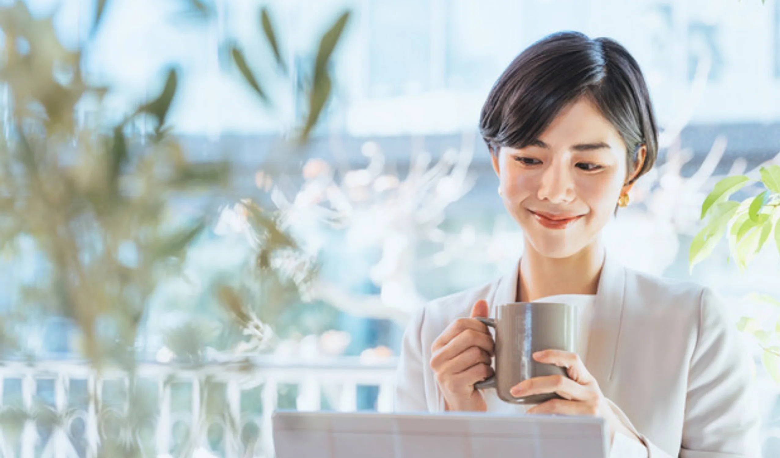 ノートパソコンの前でコーヒーを片手に落ち着いた表情で仕事をしている女性